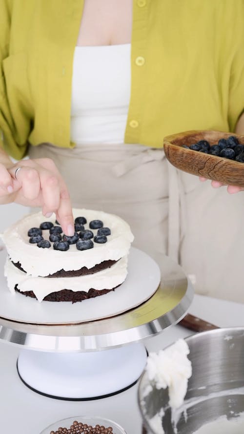 A Woman Decorating a Cake with Blueberries