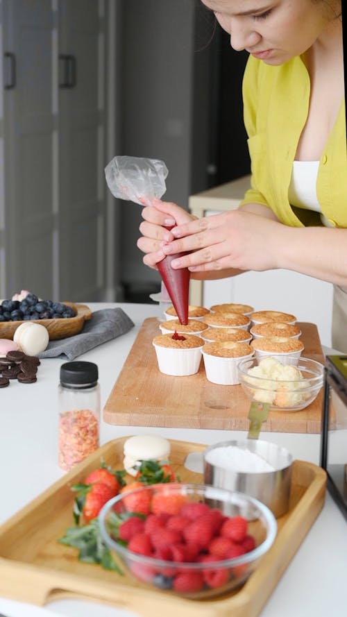 A Woman Putting Filling on the Cupcakes