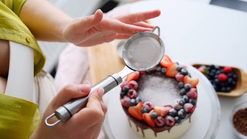 A Woman Sifting Powedered Sugar on a Cake