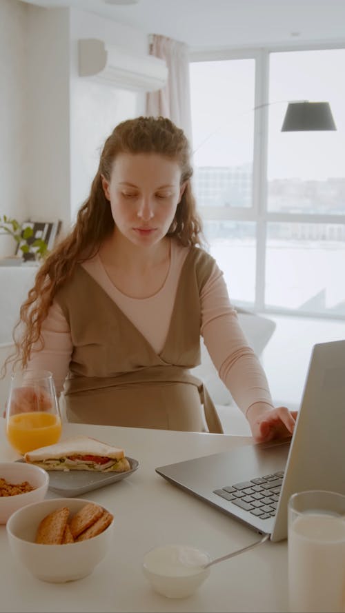 Pregnant Woman Drinking Juice While Using A Laptop