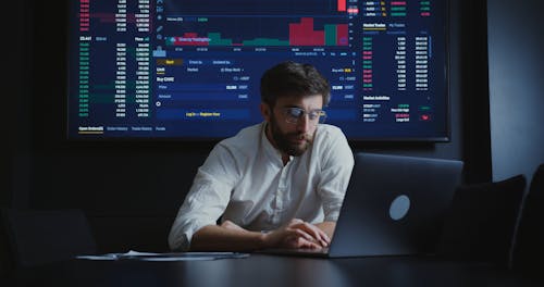 A Man Scrolling on His Laptop Behind a Big Screen