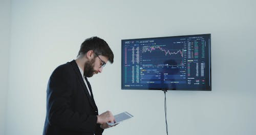 A Man Tapping on His Tablet While Looking at the Monitor