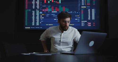 Man In Front of a Big Screen Using his Laptop