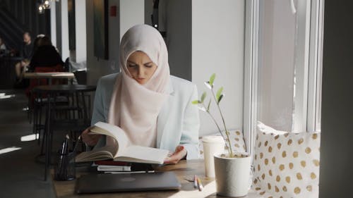 Female Wearing a Hijab Reading Book in a Coffee Shop
