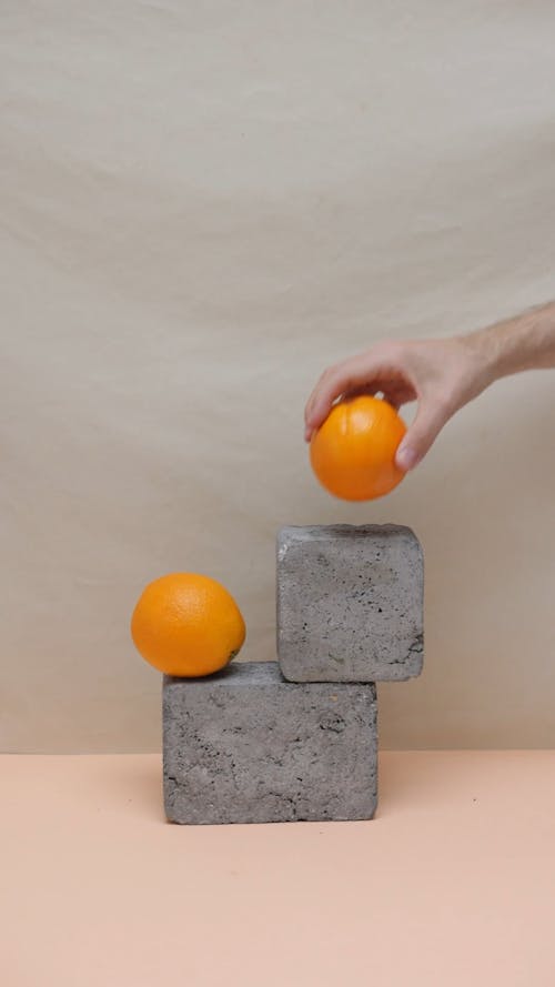 A Person Arranging Oranges on Stone Blocks