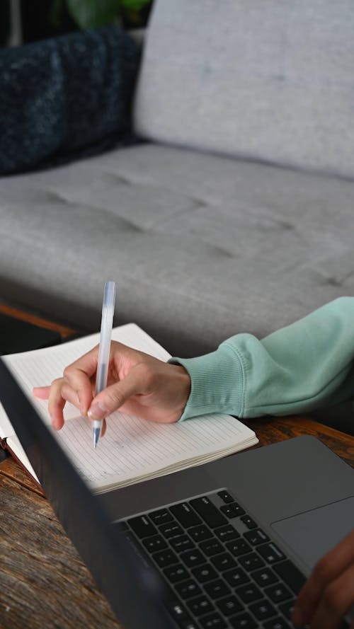 Close-Up View of a Person Writing while Using a Laptop