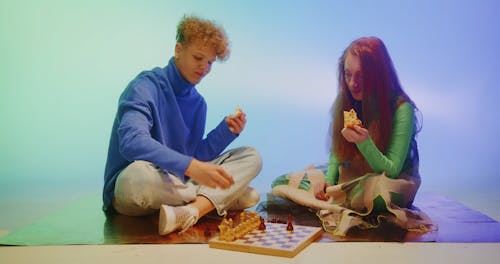 A Couple Playing Chess while Eating Pizza