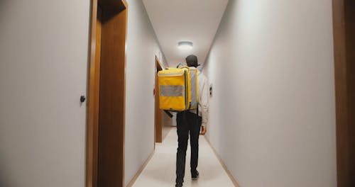 A Delivery Man Walking in the Hallway while Carrying a Thermal Bag