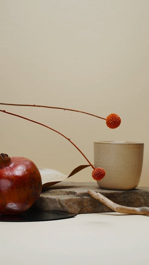 Pomegranate and Flowers Beside a Mug and a Wood