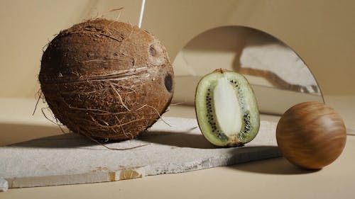 A Coconut and a Sliced Kiwi With a Rolling Ball Made of Wood