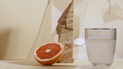 A Person Putting a Rosemary on a Glass of Water and Sliced Lemon Beside a Grapefruit