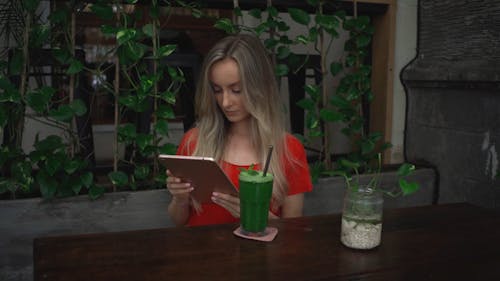 Woman Looking at Tablet and Drinking Green Juice