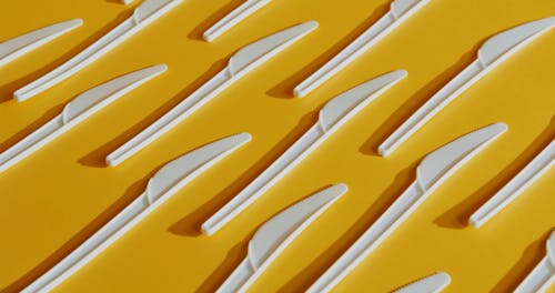 Plastic Knives Neatly Arranged on a Yellow Surface
