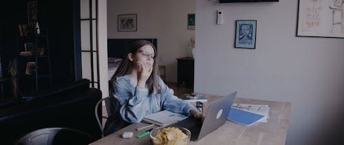 Woman Eating Chips while Using a Laptop at Home