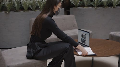 A Woman Looking at a Document and Using a Laptop