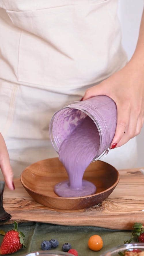 A Person Pouring Smoothie in a Wooden Bowl 