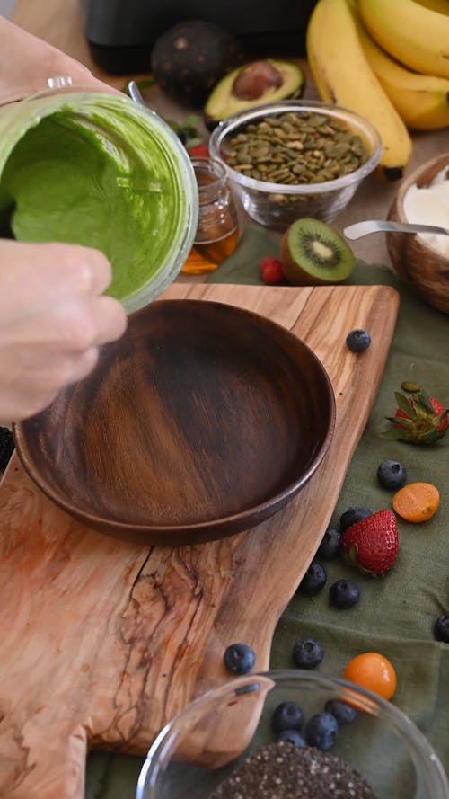 A Person Pouring a Smoothie in a Wooden Bowl 
