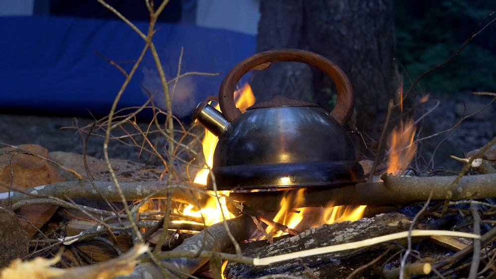 Two People In Front Of A Campfire Pouring Water From A Kettle · Free