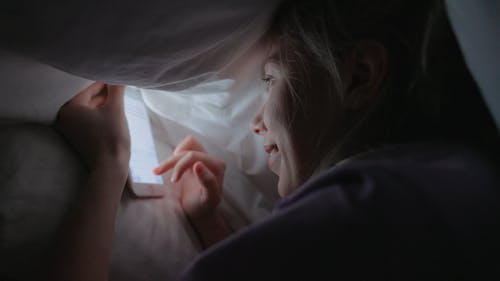 A Woman Using Cellphone Under the Blanket