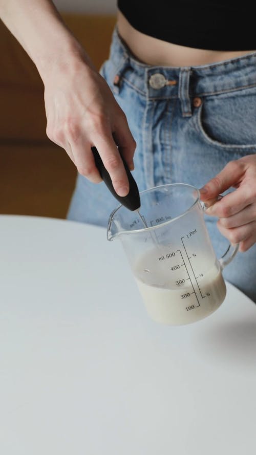 A Person Whisking Milk in a Glass Jug