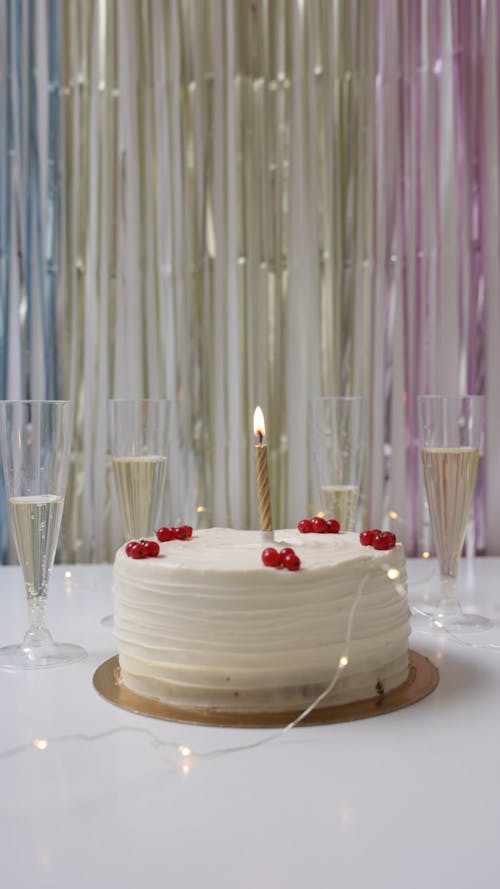 A Cake with a Candle and Glasses of Champagne on the Table