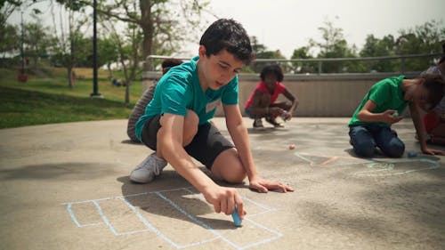 A Little Boy Making Art on the Ground with Chalk
