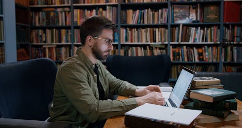 A Man Looking at Documents and Typing on a Laptop