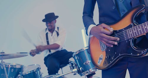A Man Playing the Drums While Another Man is Playing the Guitar