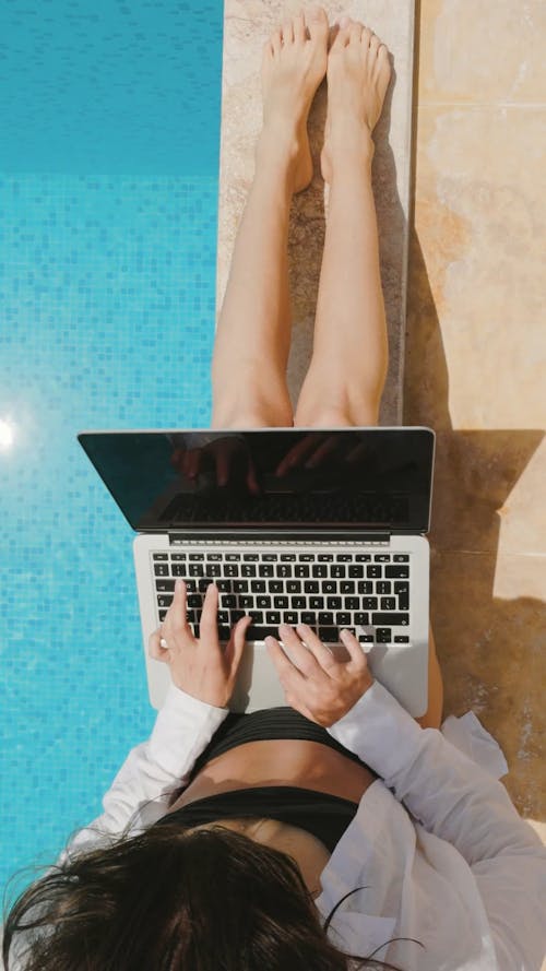 Woman Sitting On Poolside And Using A Laptop