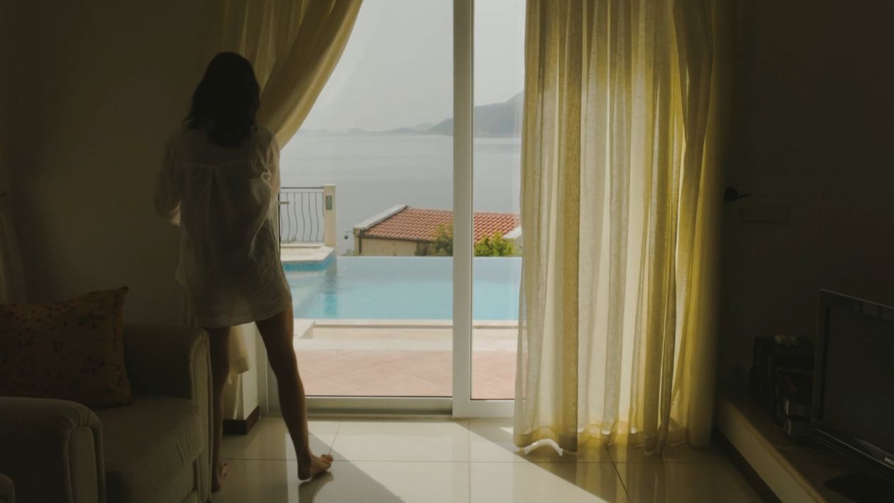 A guest opens the curtains to a view of the pool and sea
