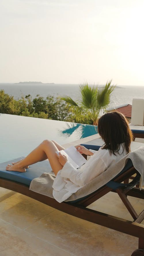 Woman Sitting Near the Pool and Reading a Book