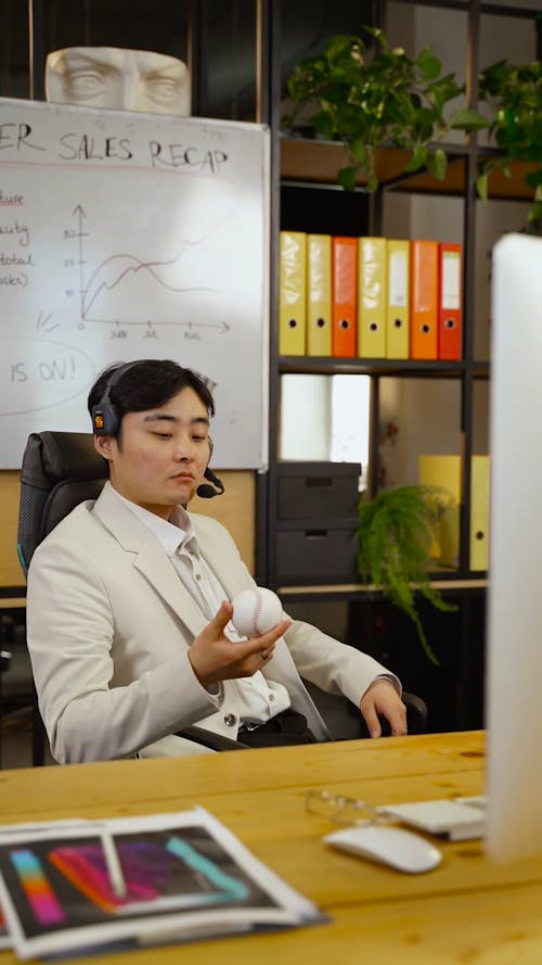 A Man in a Headset Playing with a Baseball in an Office