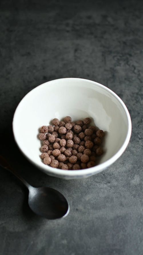 A Person Putting Chocolate Cereals with Milk in a Bowl