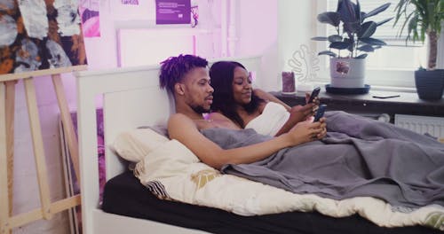 A Couple Using Their Phone while Lying on Bed