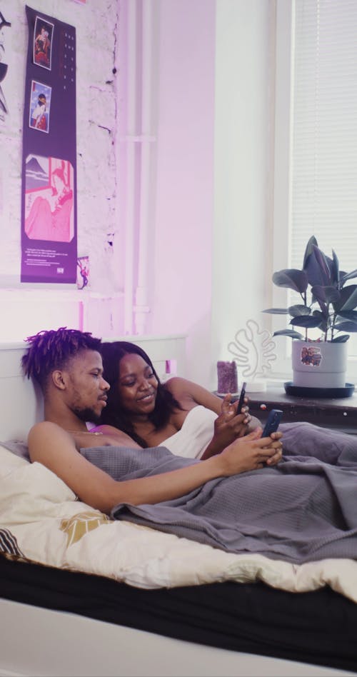 Couple Lying on Bed While Using Cellphone