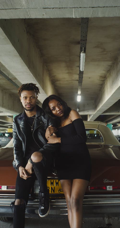 A Couple Leaning on a Car Behind Them While Looking at the Camera