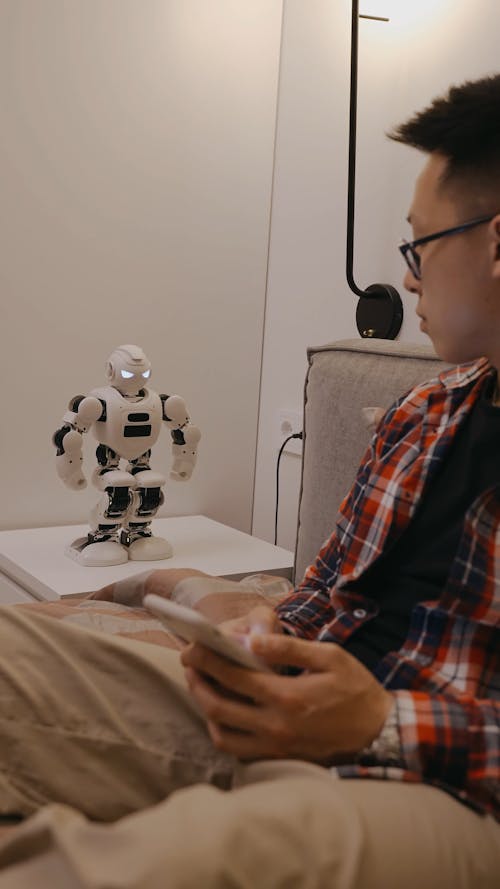 A Man Holding His Phone while Playing with the Robot