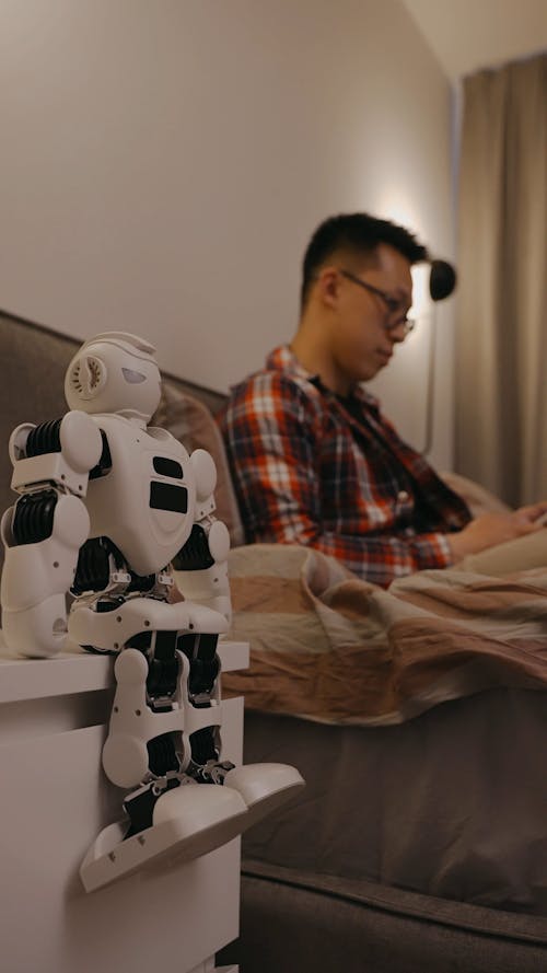 Robot Sitting On a Table Beside a Bed