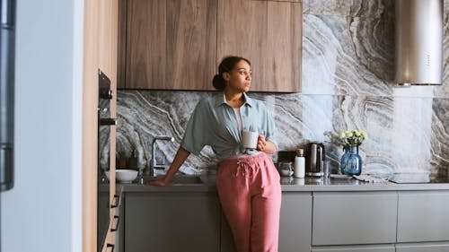 Woman Holding a Coffee Mug while Standing in the Kitchen