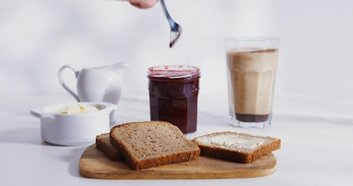 A Person Spreading Strawberry Jam on a Bread