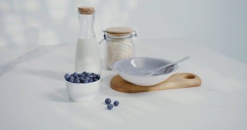 A Bowl with Spoon and a Cup of Blueberries, Bottle of Milk and Oatmeal