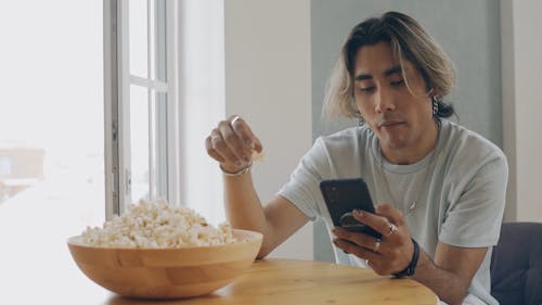 Man Eating Popcorn while Browsing on his Phone