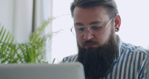 A Bearded Man Removing Eyeglasses while Working