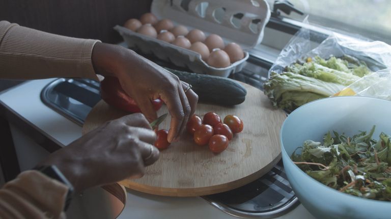 Hands slicing tomatoes and vegetables on a cutting board for meal prep