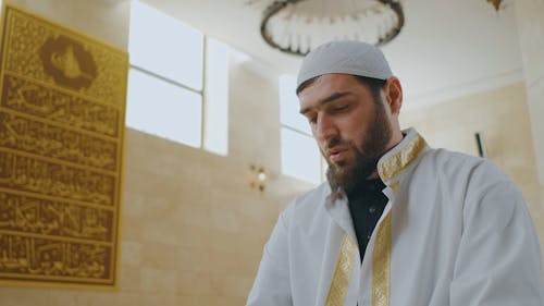 A Man Praying while Looking at the Quran Book