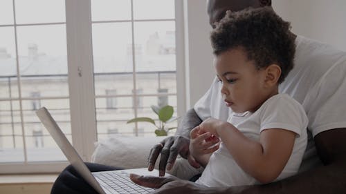 A Father Using a Laptop while Carrying His Son