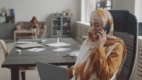 A Woman Typing on a Laptop while Having a Phone Call