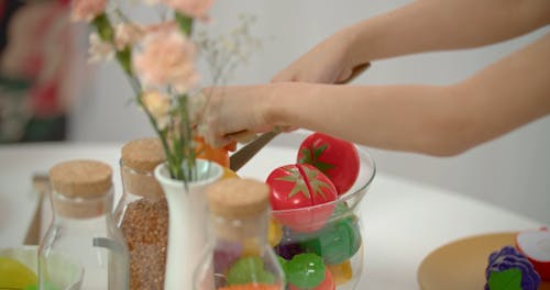 A Child Cutting Toy Fruits with a Fork and Knife