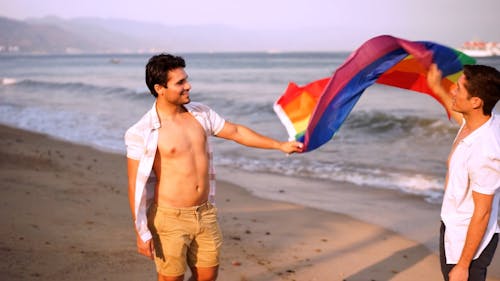 A Couple Holding a Rainbow Flag at the Beach