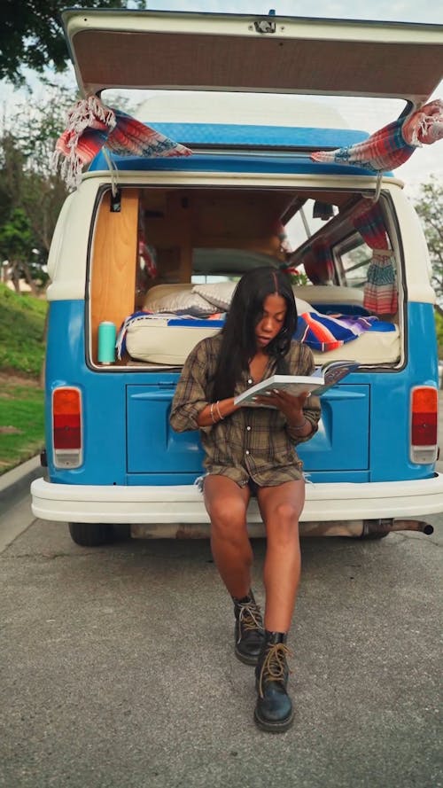 Woman Reading a Book while Sitting on a Camper Van